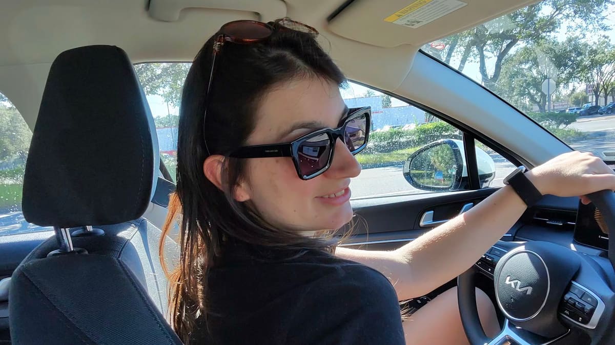 Camila, da Desenrola, ao volante de um carro alugado em Orlando, de óculos escuros e sorrindo