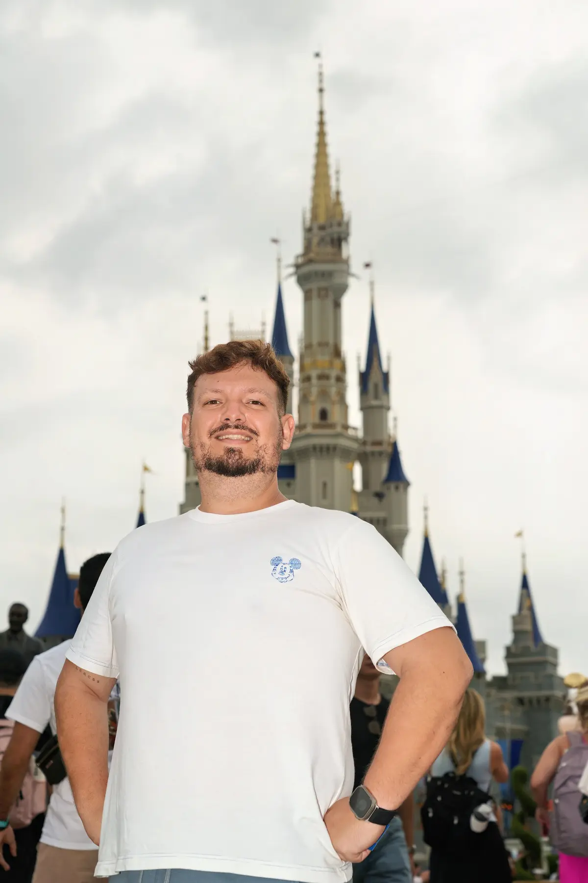Thomaz, guia da Desenrola, sorri com as mãos na cintura diante do Castelo da Cinderela, no Magic Kingdom