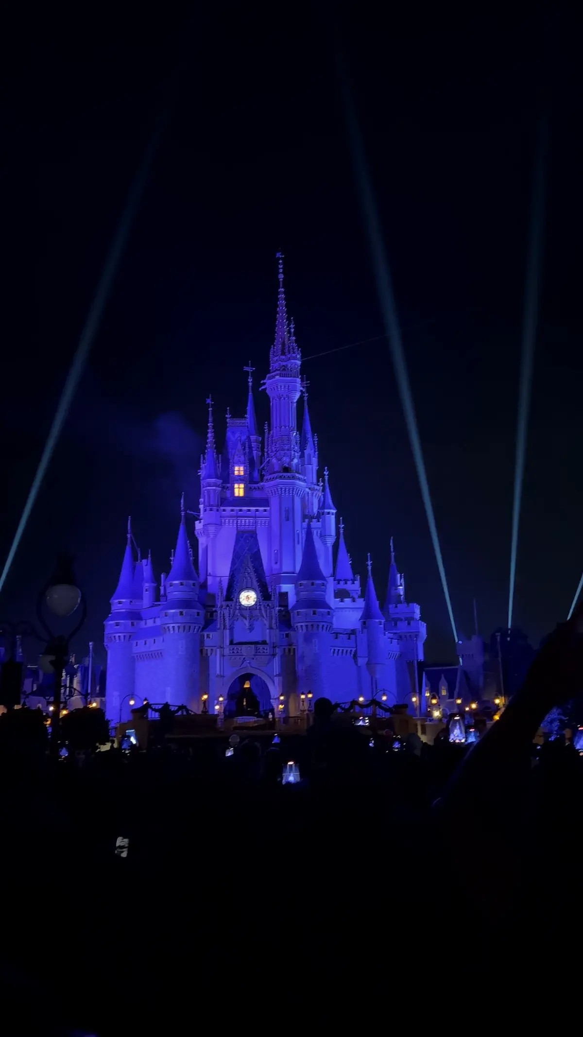 Castelo da Cinderela iluminado de azul à noite, com fachos de luz no céu, no Magic Kingdom