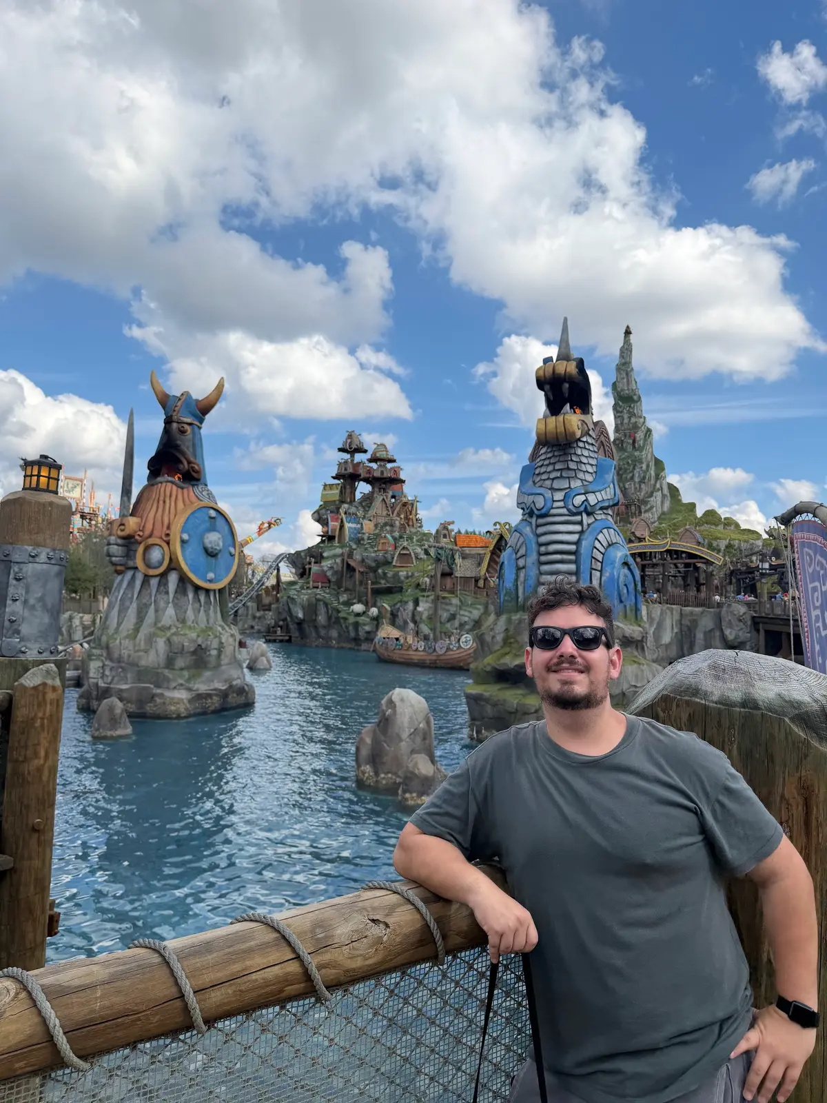 Thomaz apoiado na cerca da lagoa da Isle of Berk, com estátuas vikings ao fundo, no Epic Universe