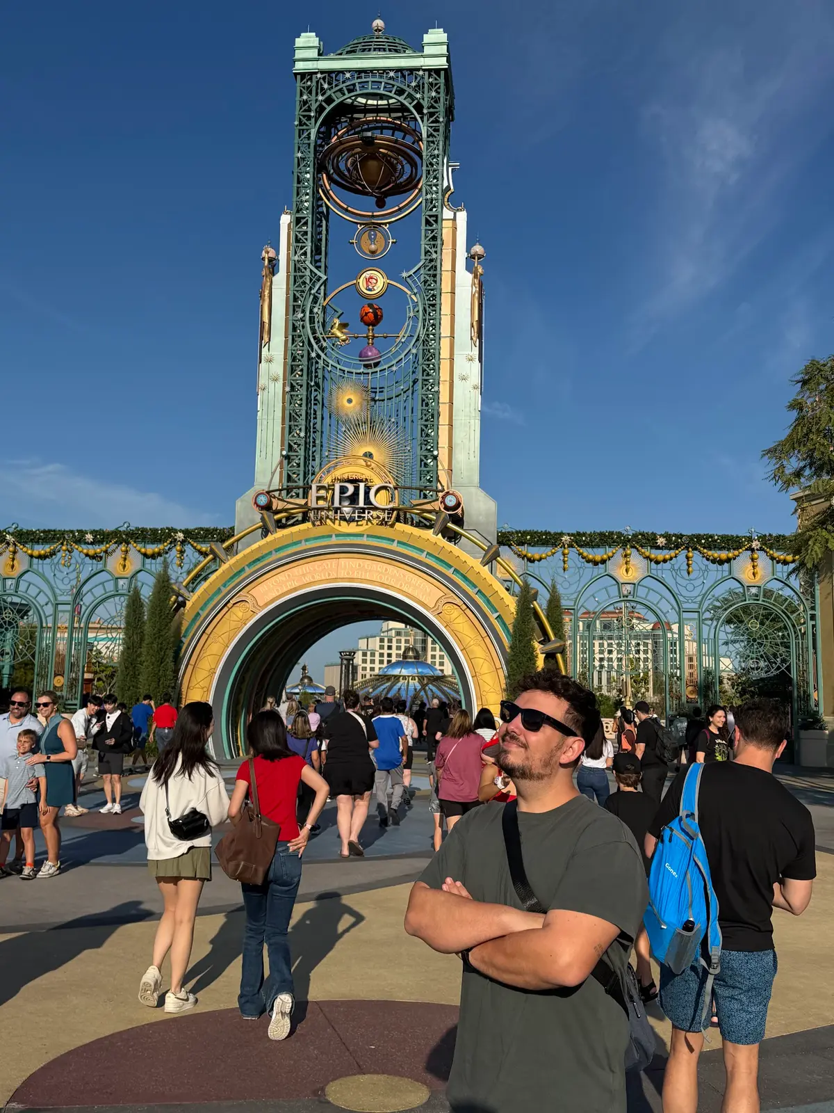 Thomaz de braços cruzados diante da torre Chronos, no portal de entrada do Epic Universe, na Universal Orlando