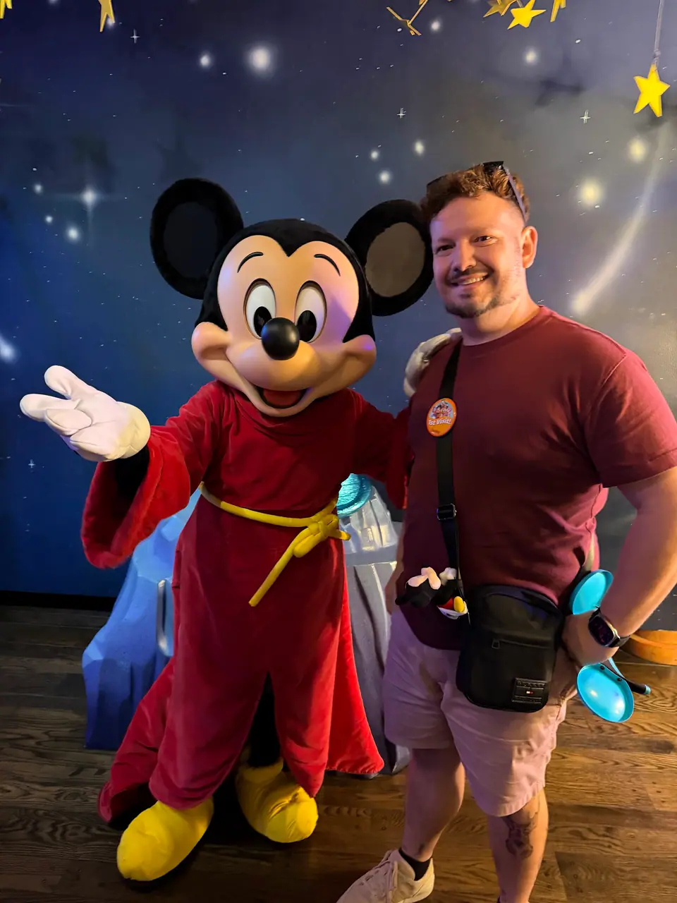 Thomaz abraçado ao Mickey Aprendiz de Feiticeiro (Fantasia), ambos sorrindo diante de fundo estrelado